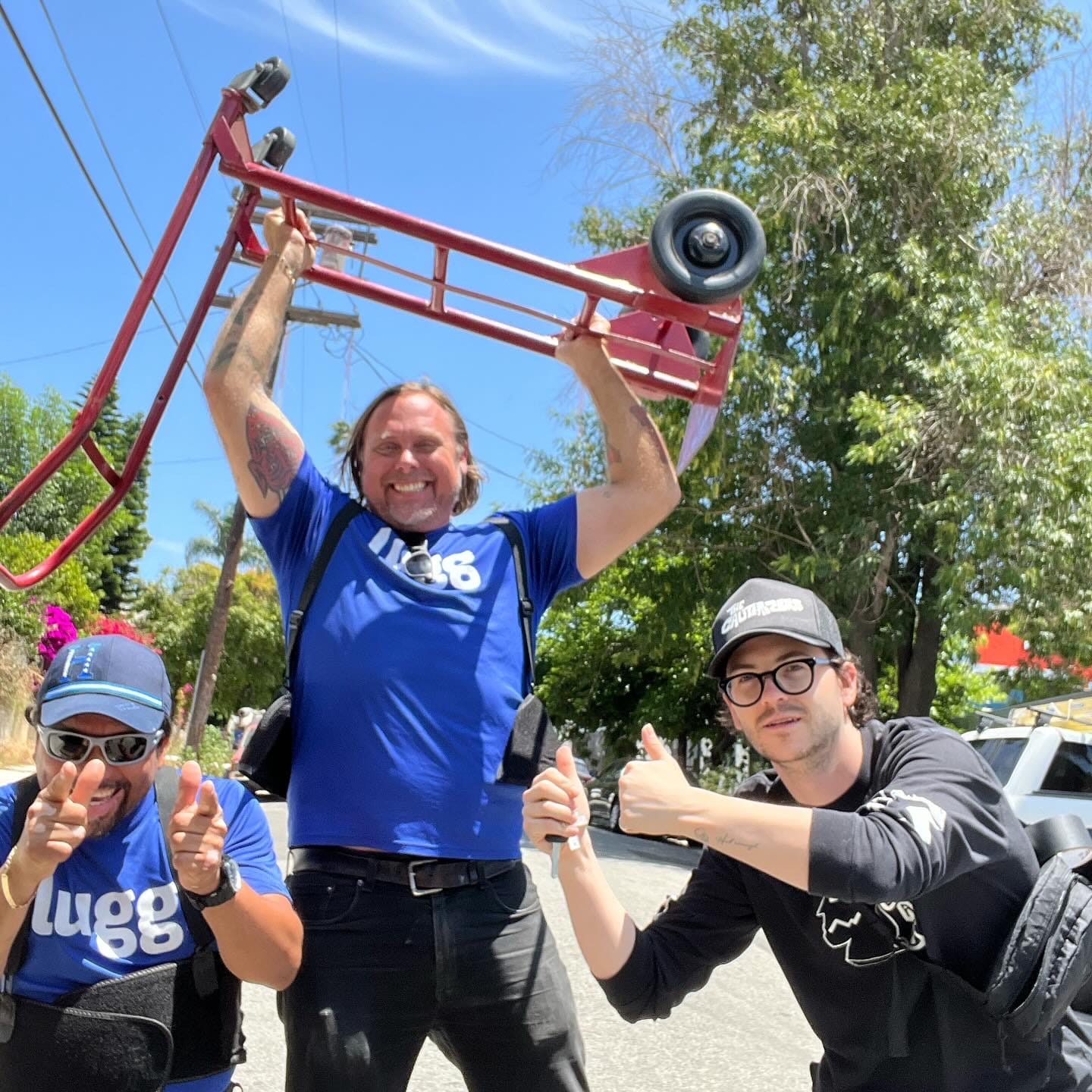 Two Lugg movers smiling and posing with a customer after a completed move, holding a red dolly under bright summer skies.