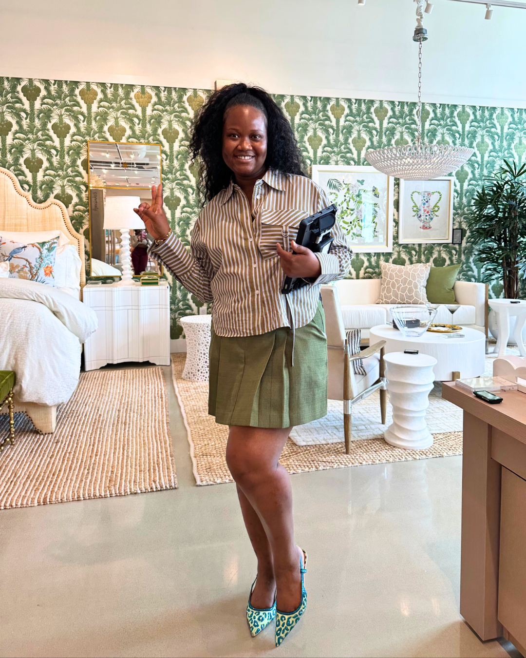 Lagbeh, a Perigold Houston associate, smiling and holding a tablet while standing in front of a fully styled luxury bedroom vignette.