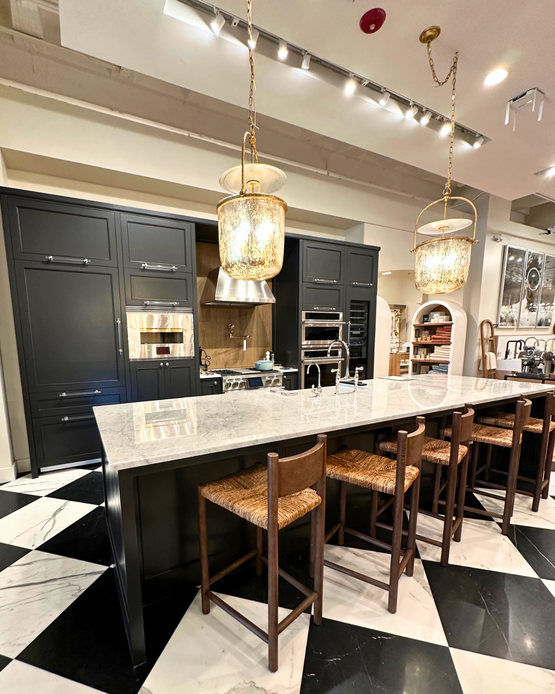 Luxury kitchen display at Perigold Houston with black cabinetry, marble countertops, oversized pendant lights, and a checkerboard floor.