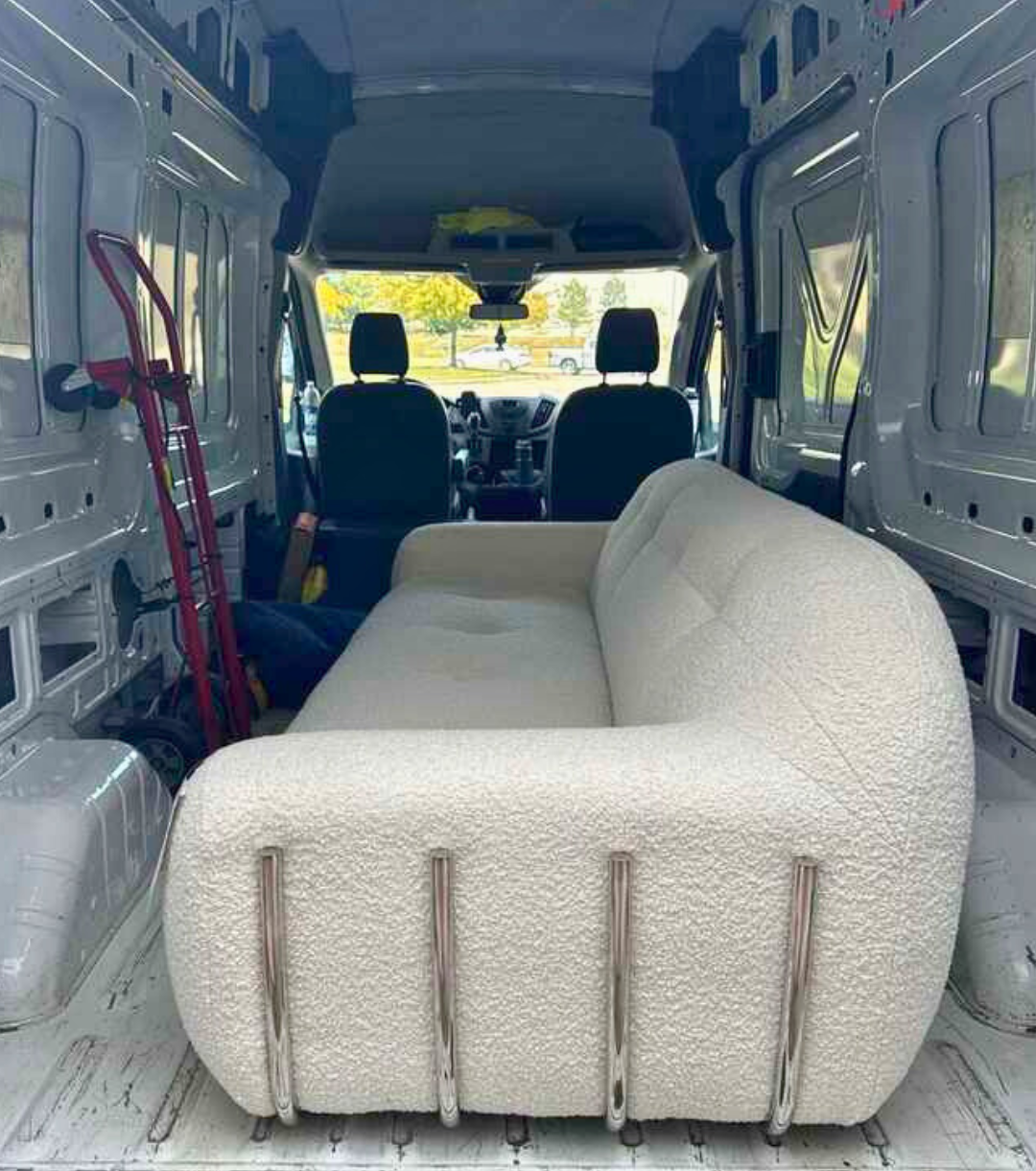 A textured ivory CB2 boucle couch sits inside a high-roof cargo van, positioned neatly against the van wall with a red dolly nearby, ready for residential furniture delivery.