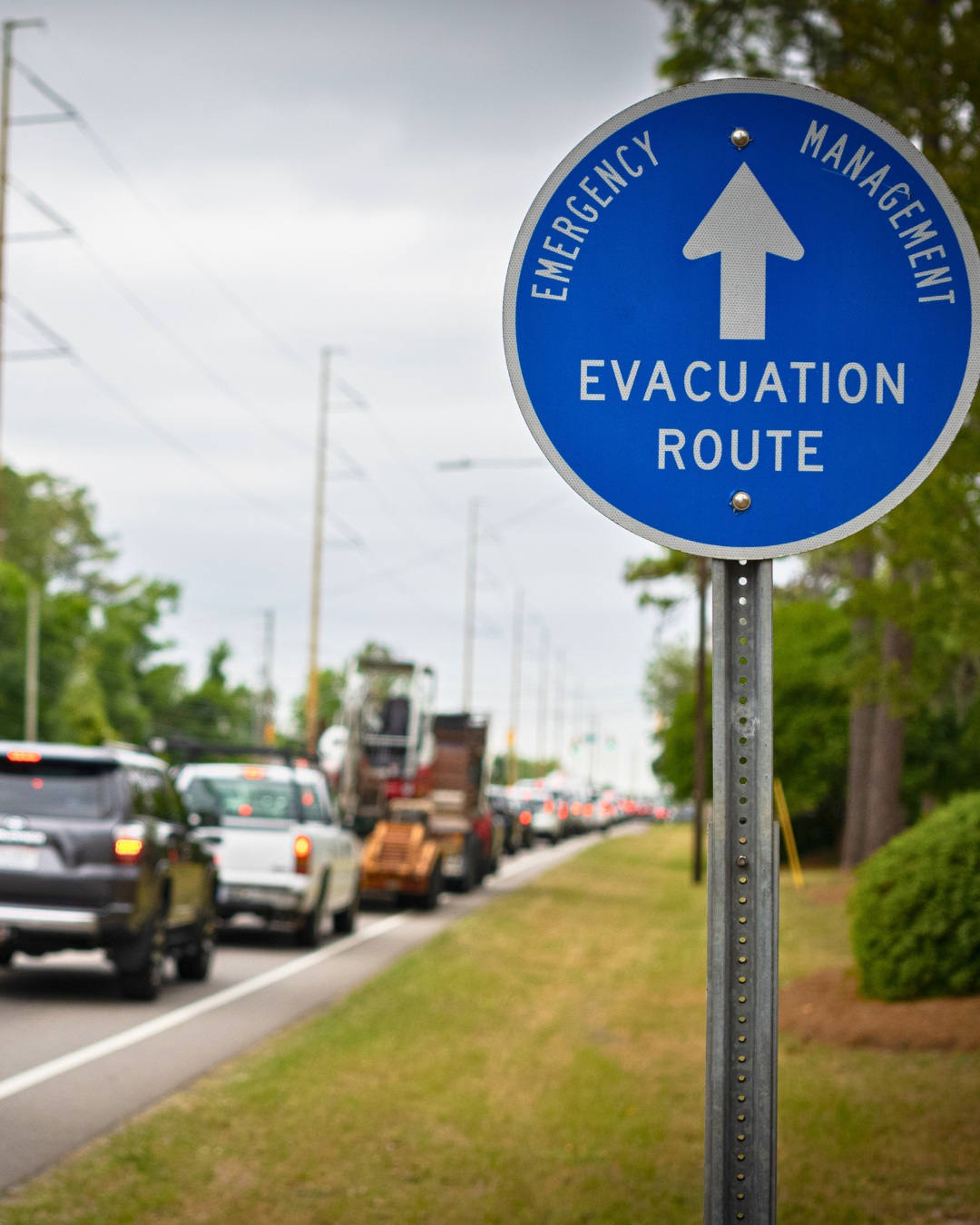 Emergency evacuation route sign along a busy road with cars in traffic during a hurricane warning.