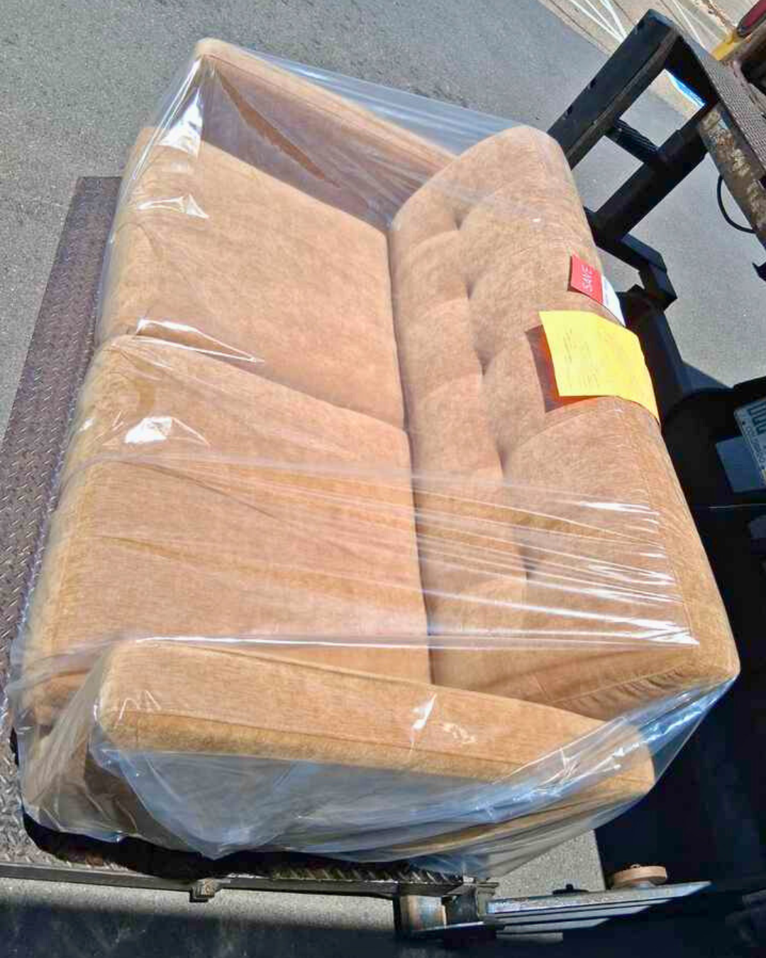 Tan tufted couch from Living Spaces wrapped in plastic and loaded onto a moving lift for same-day furniture delivery.