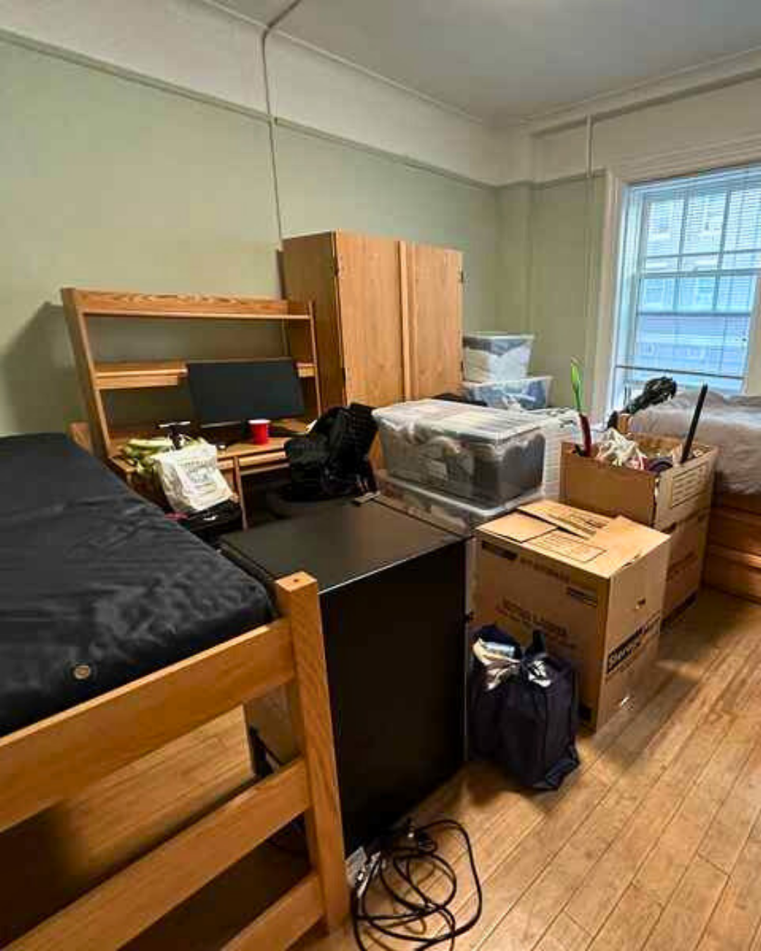 A college dorm room filled with moving boxes, furniture, and personal items.