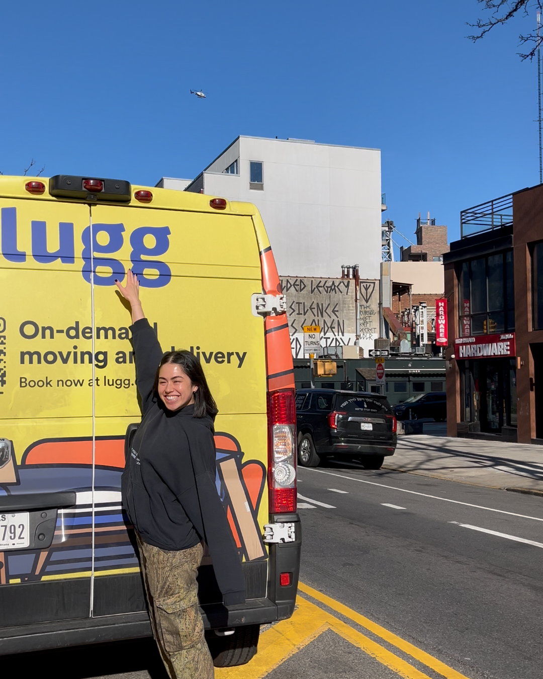 Smiling customer pointing at the back of a yellow Lugg van on a sunny NYC street.