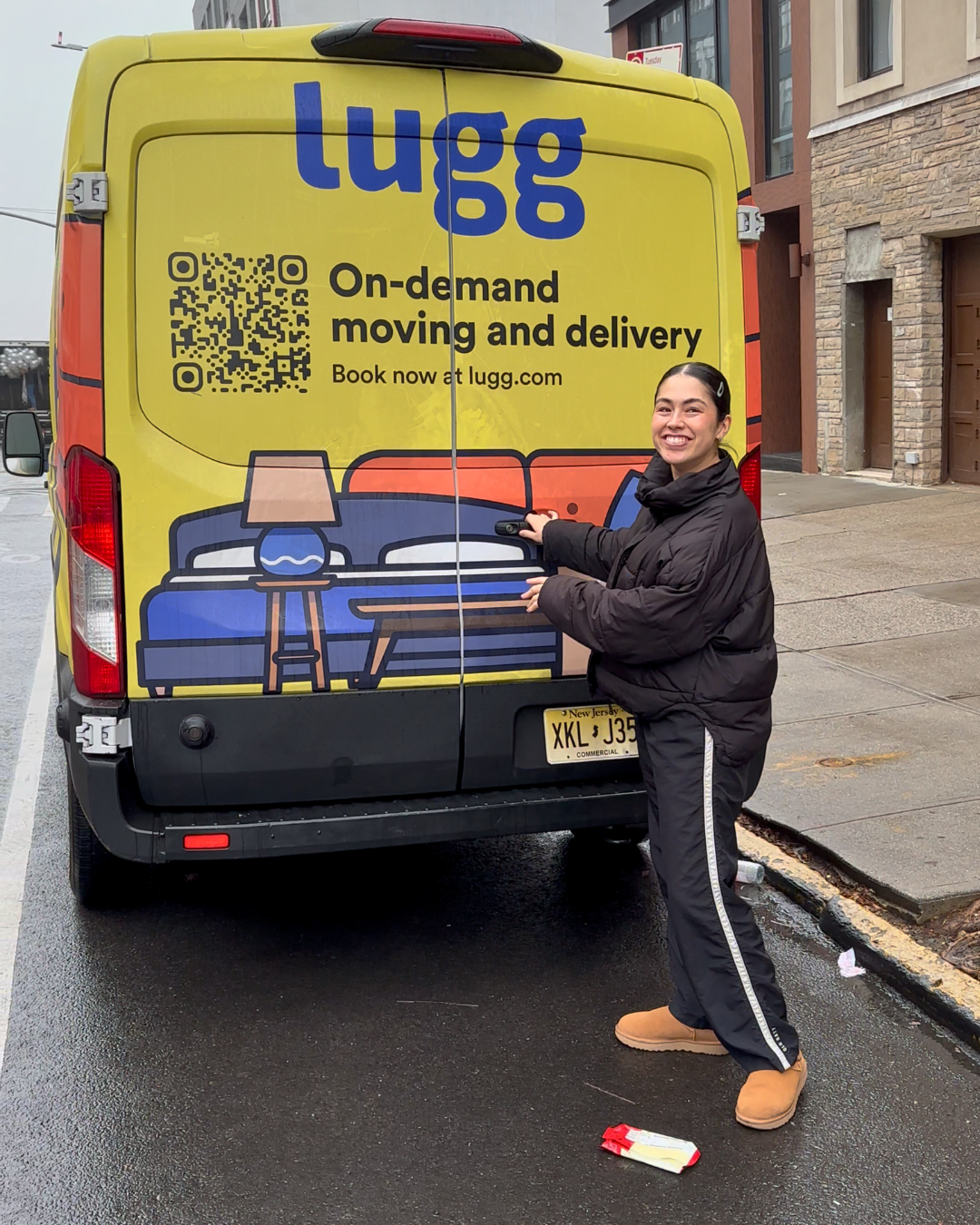 A smiling customer standing behind a yellow Lugg truck on a New York City street after her same-day furniture delivery.