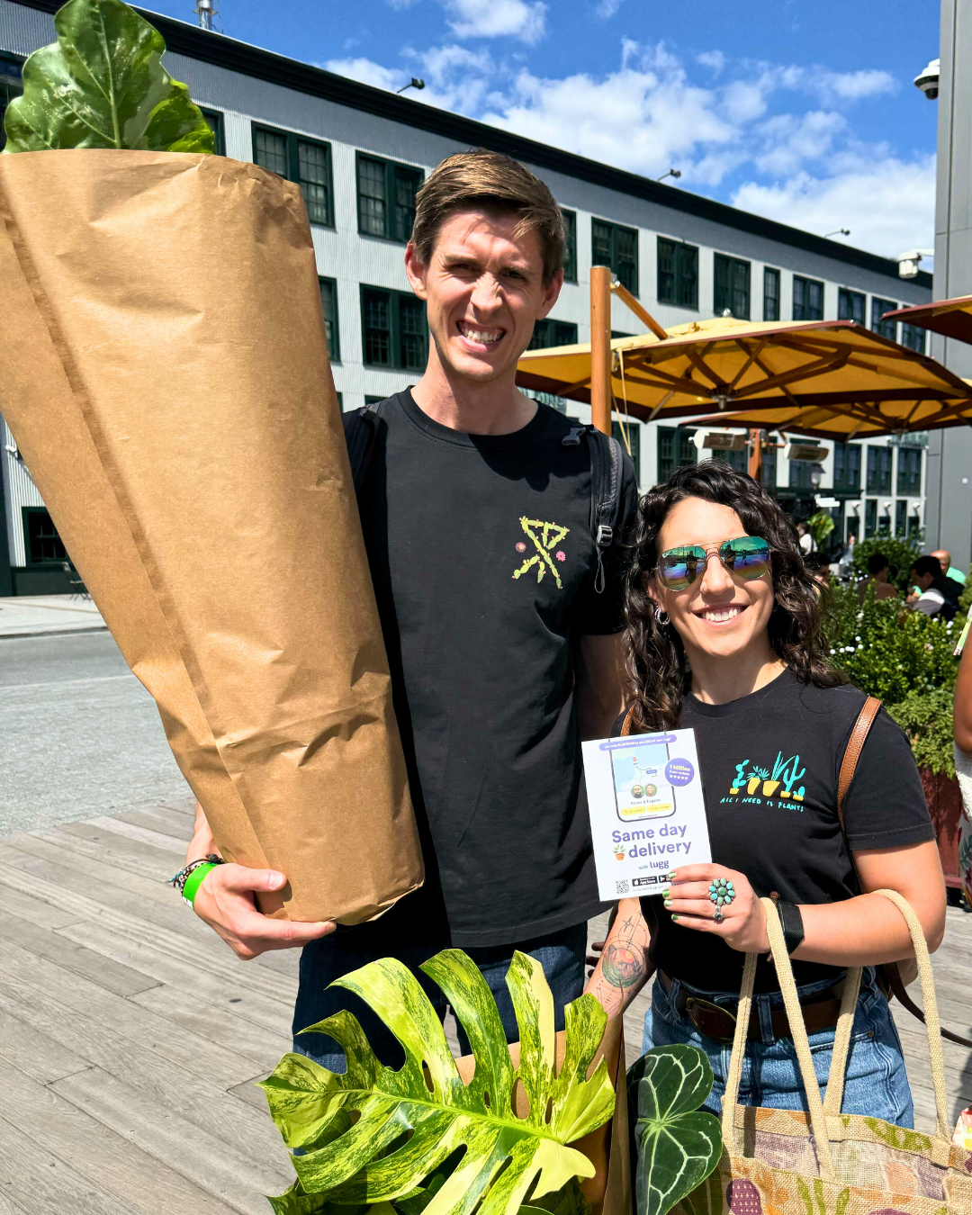 A couple at PlantCon NYC holding a large wrapped plant and a Lugg same-day delivery flyer.