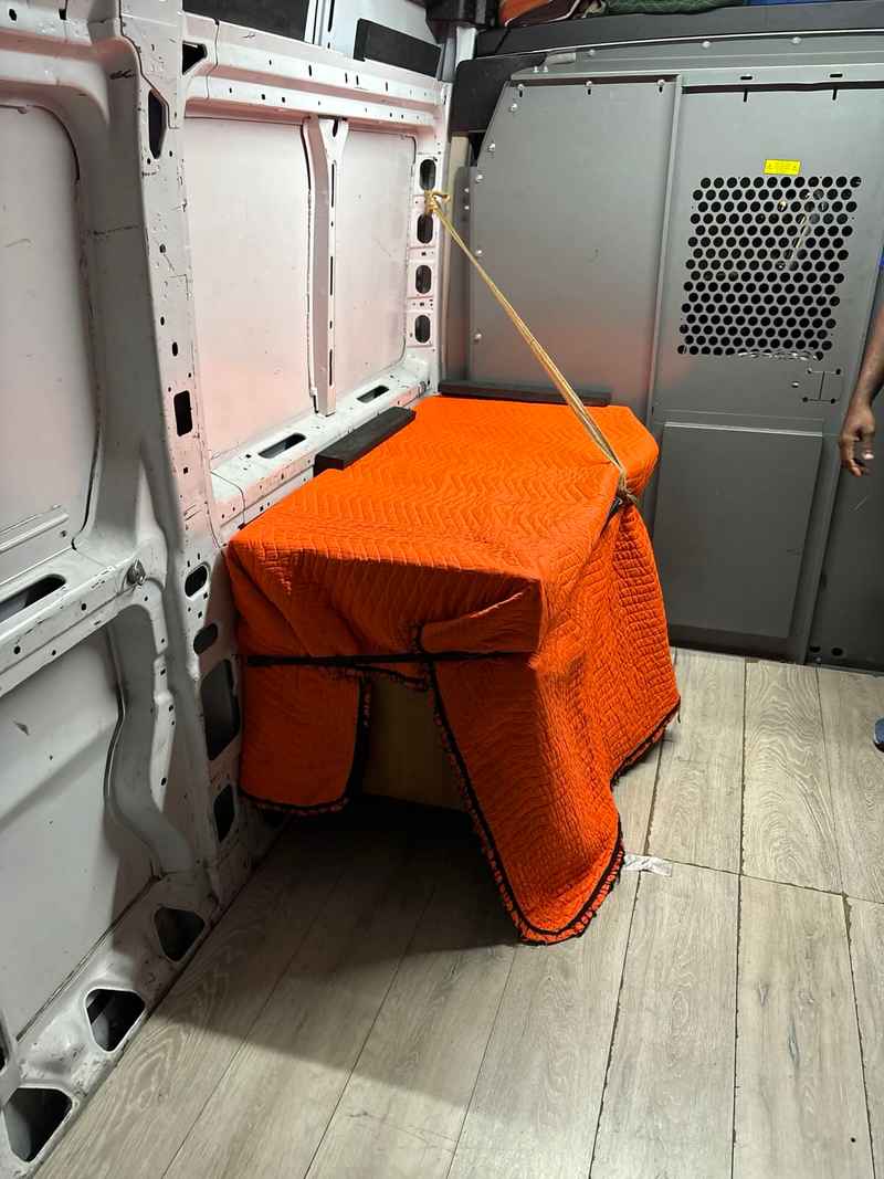 Furniture wrapped in an orange moving blanket and strapped inside a delivery van for safe transport.