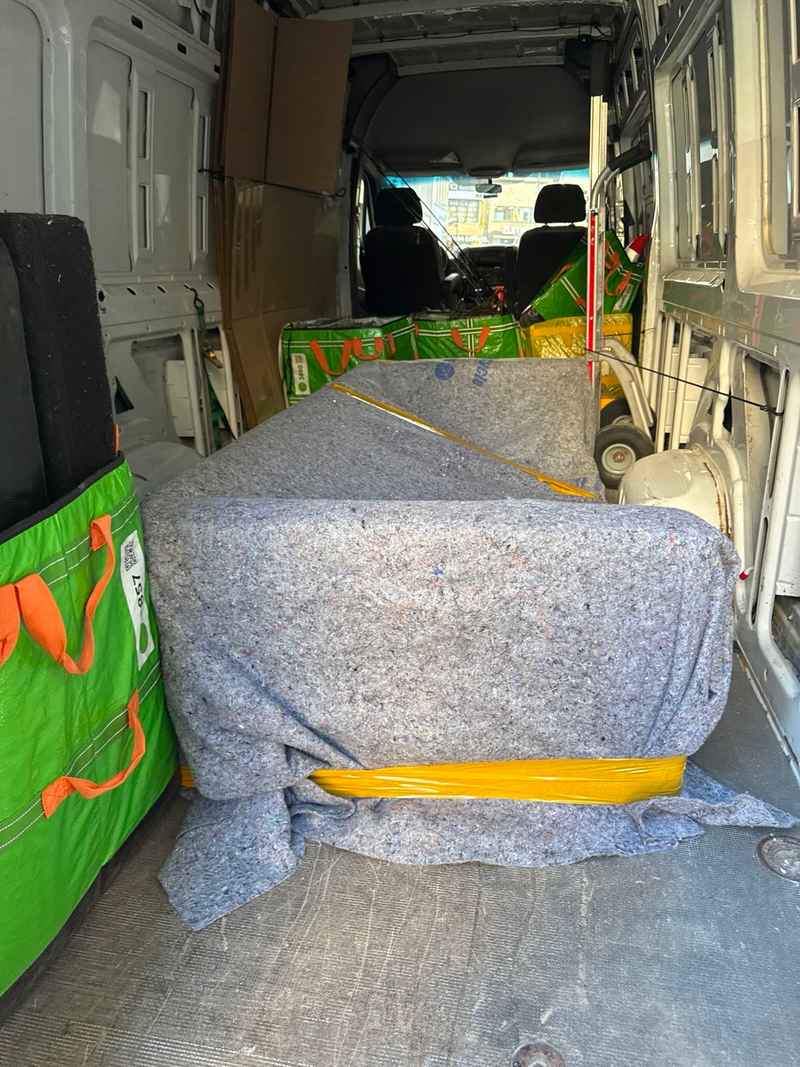 A couch covered with a gray protective blanket and yellow strap inside a moving van during local delivery.