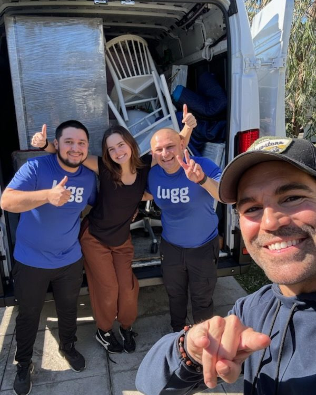 Two Lugg movers smiling with a customer in front of a van full of packed furniture.