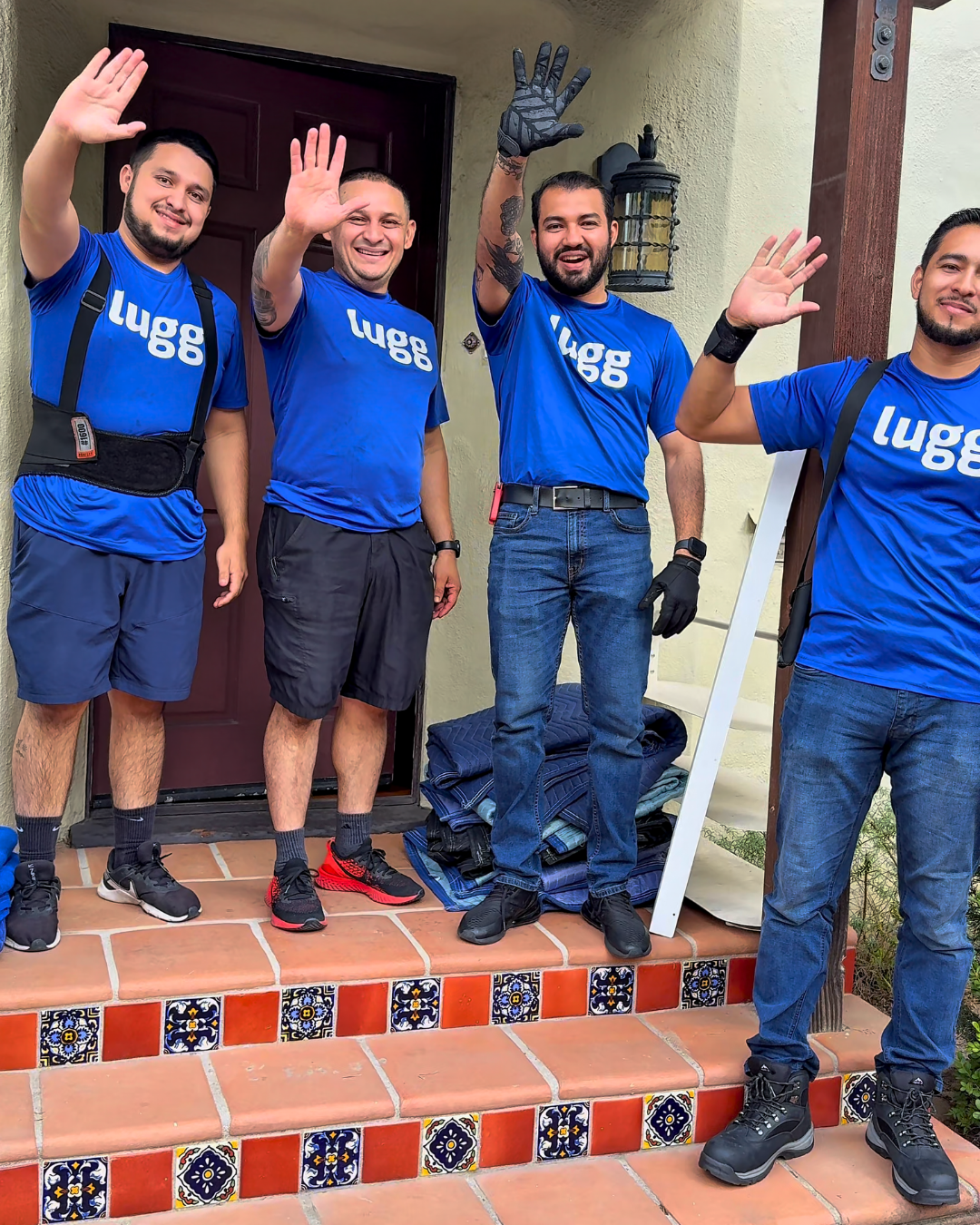 Four smiling Lugg movers wave outside a customer’s home, showing friendly, professional support for a stress-free move.