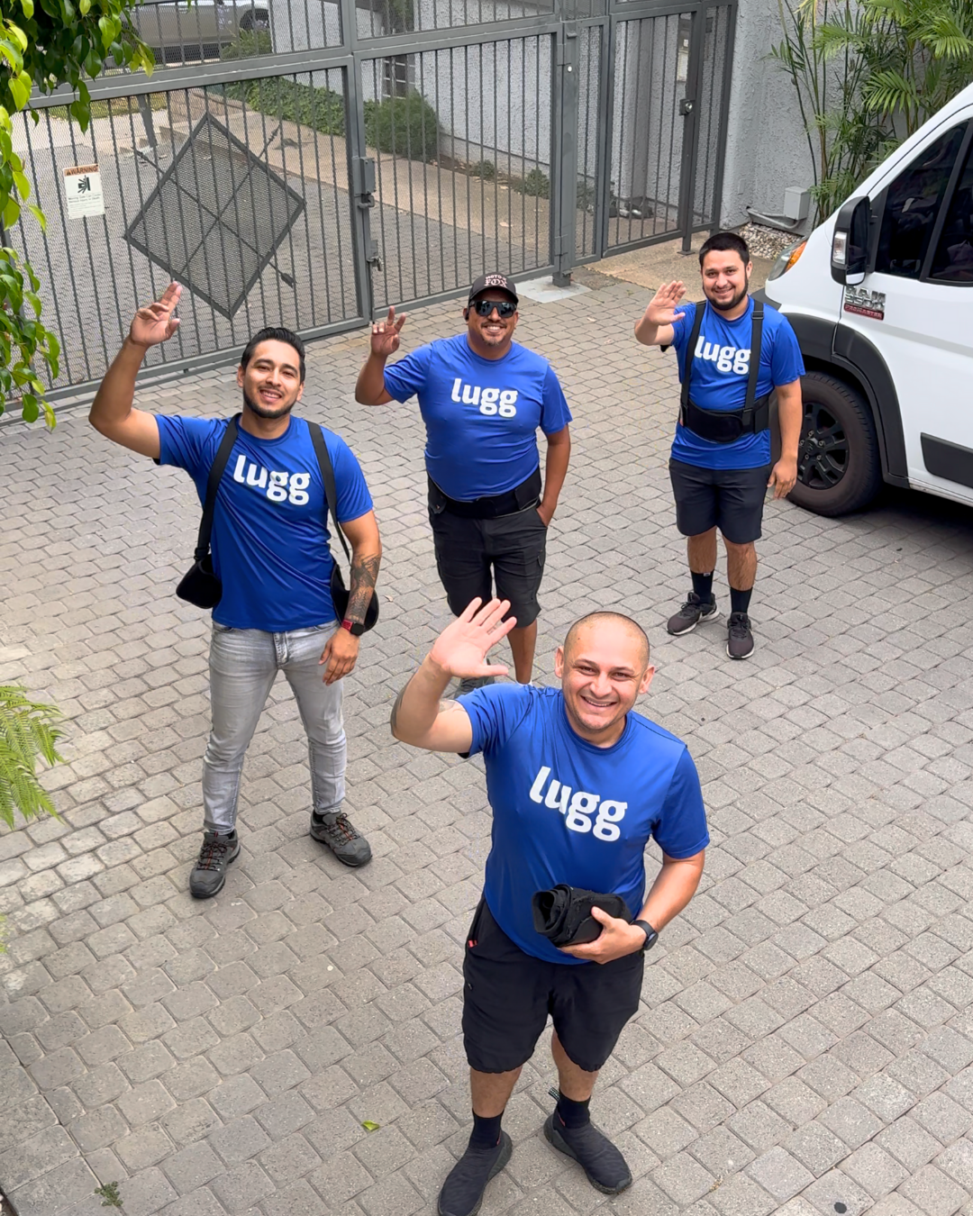 Four Lugg movers in blue shirts waving outside next to a Lugg van.