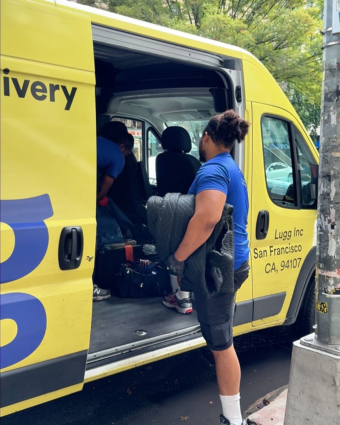 Lugg movers loading furniture into a van at the curb on a city street in the morning.