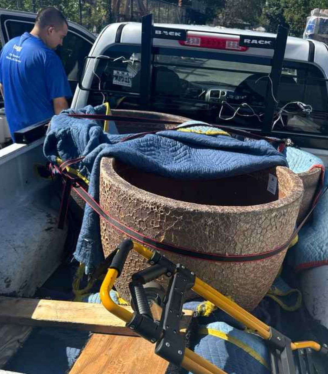 A large ceramic pot wrapped in blankets and secured with straps in a pickup truck by a Lugg driver.