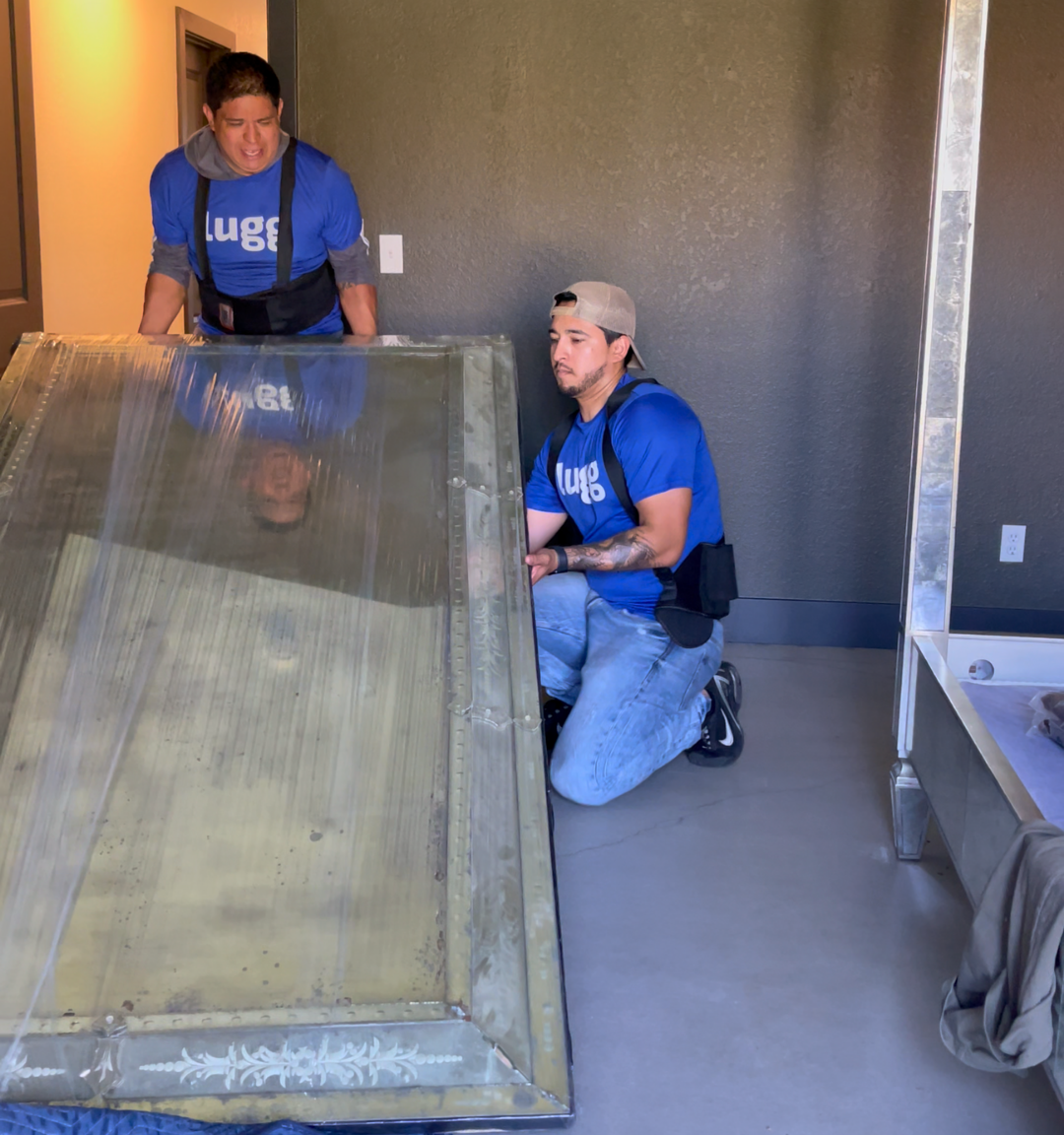 Two Lugg movers lifting and positioning a heavy framed head board indoors, demonstrating safe handling of oversized items.