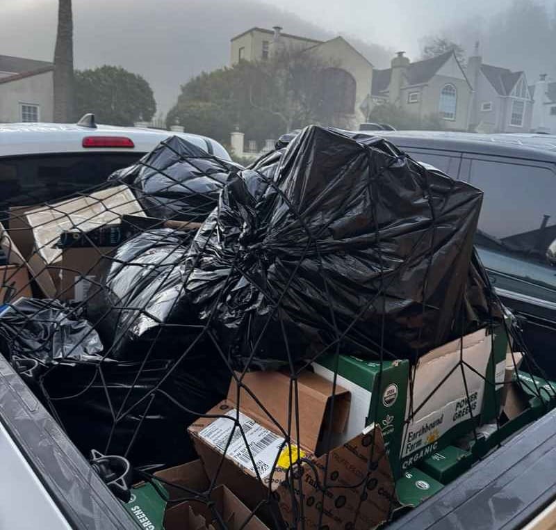 Pickup truck bed loaded with trash bags and boxes secured with a cargo net on a foggy residential street