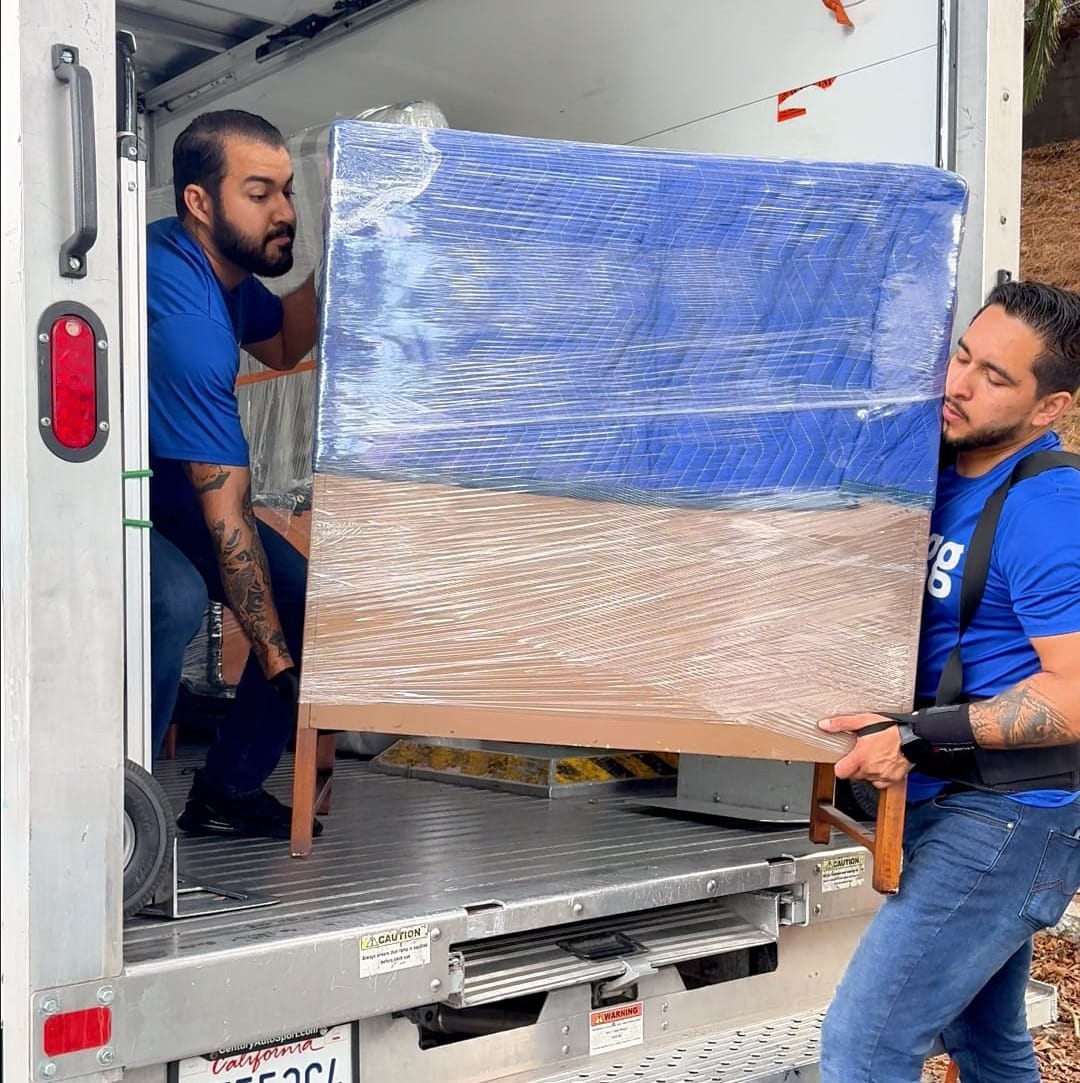 Two Lugg movers loading a stretch-wrapped dresser onto a box truck.