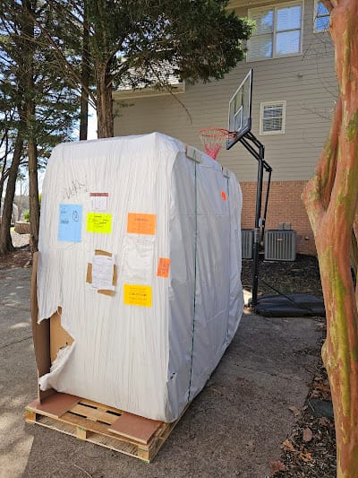 Wrapped hot tub on a pallet in a residential driveway, staged before being moved to the backyard by Lugg