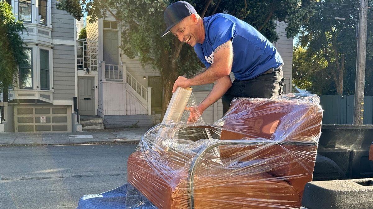 Uber for movers in action: a Lugg mover stretch-wrapping a leather armchair on a pickup truck during a residential San Francisco furniture move.