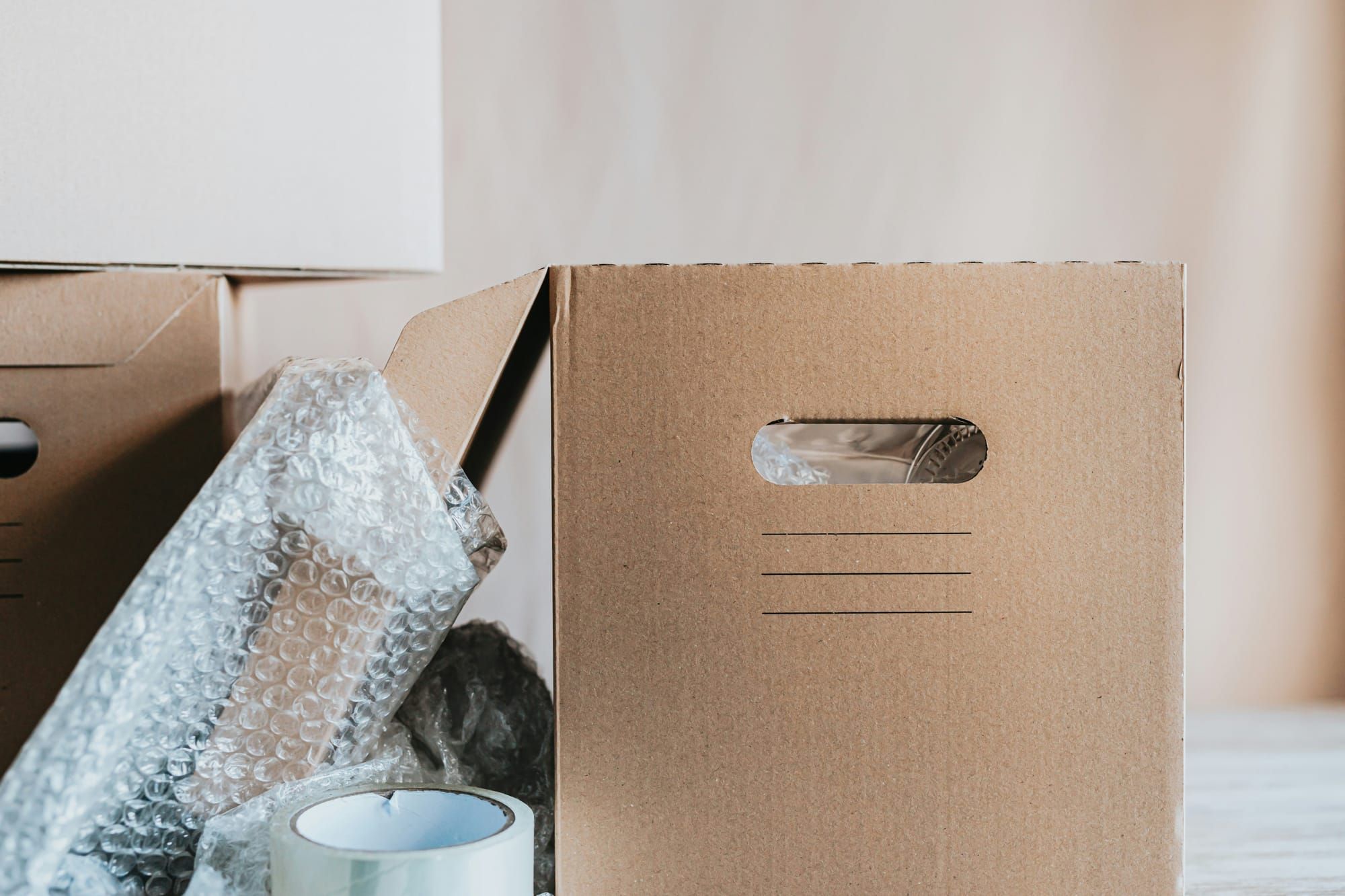 A moving box with a handle next to bubble wrap and a roll of packing tape — essential packing supplies for a move