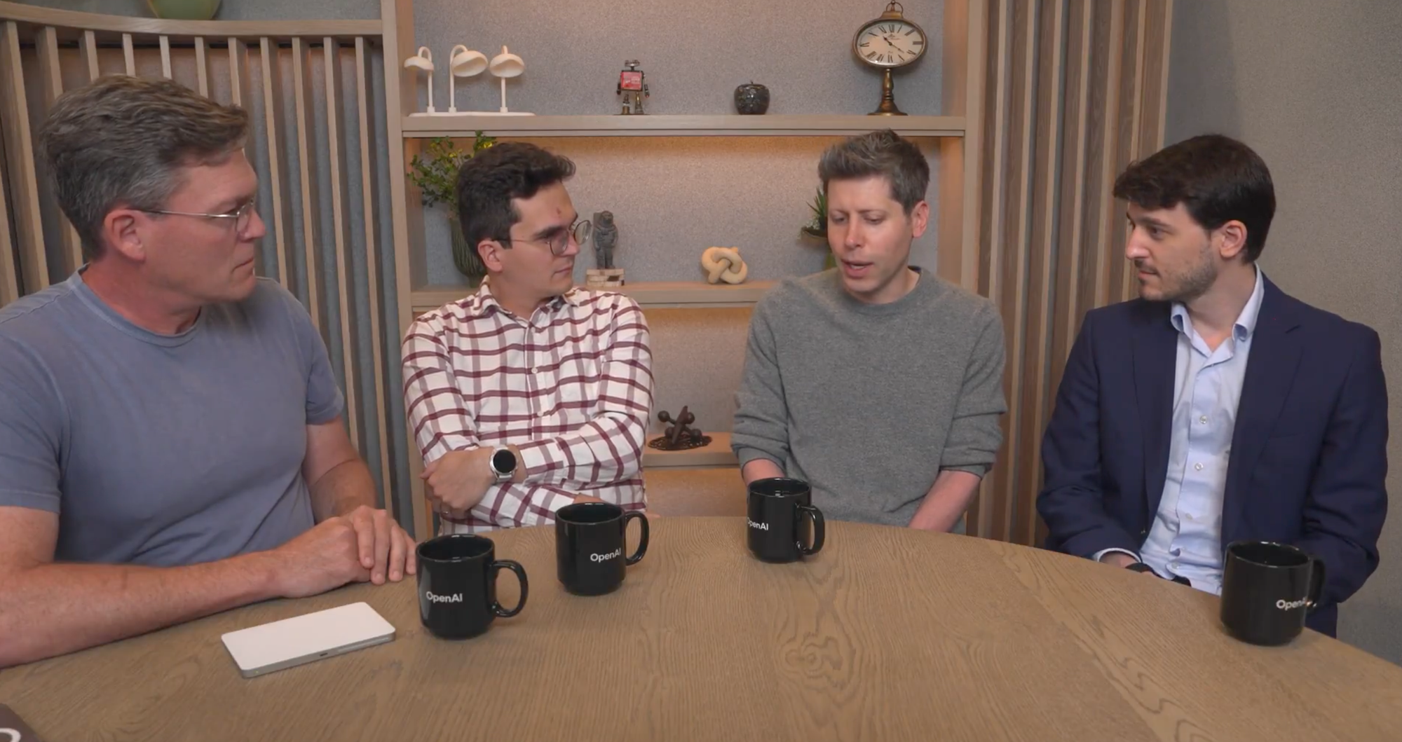 Four seamingly serious professionals from OpenAI sit gravely around a table