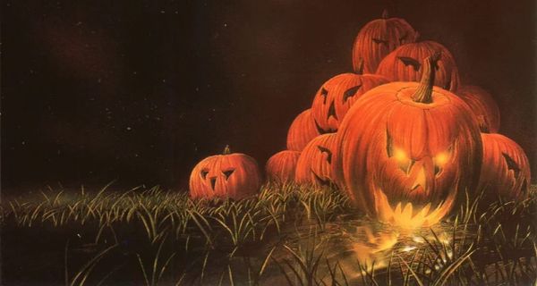 A pile of jack o' lanterns on a field at night. The one in the front has an evil grin and is lit from within.