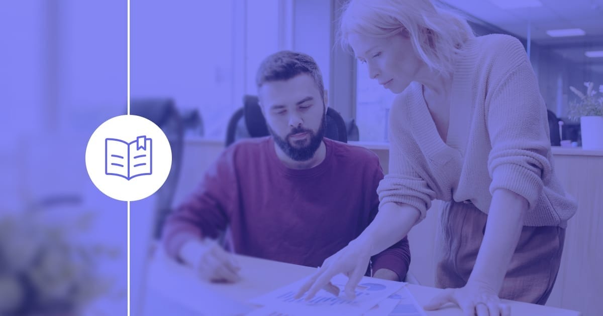 Two employees consulting the software documentation process listed in an employee handbook.