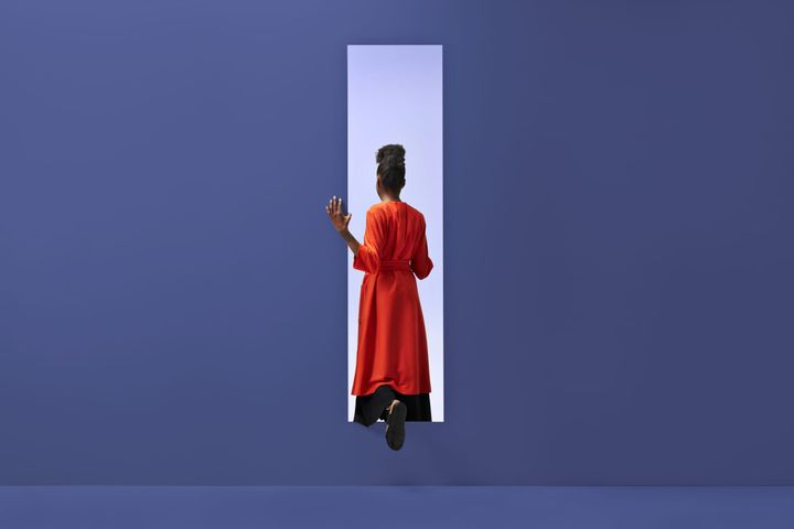 Black person with orange cloak stepping through portal in purple background