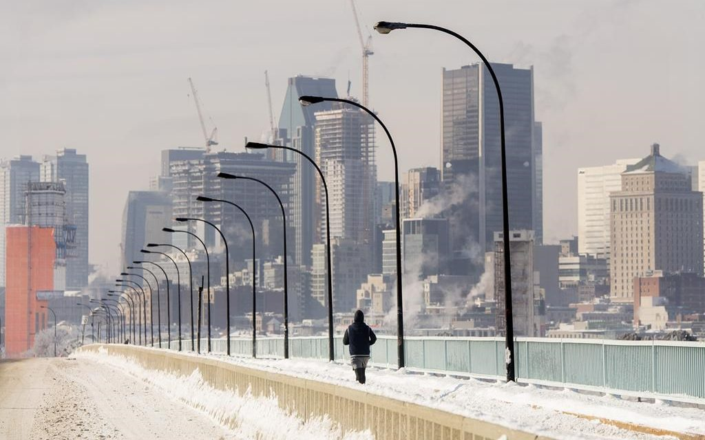 A person jogs next to a backdrop of the Montreal skyline as ice fog rises off the St. Lawerence River in Montreal, Saturday
