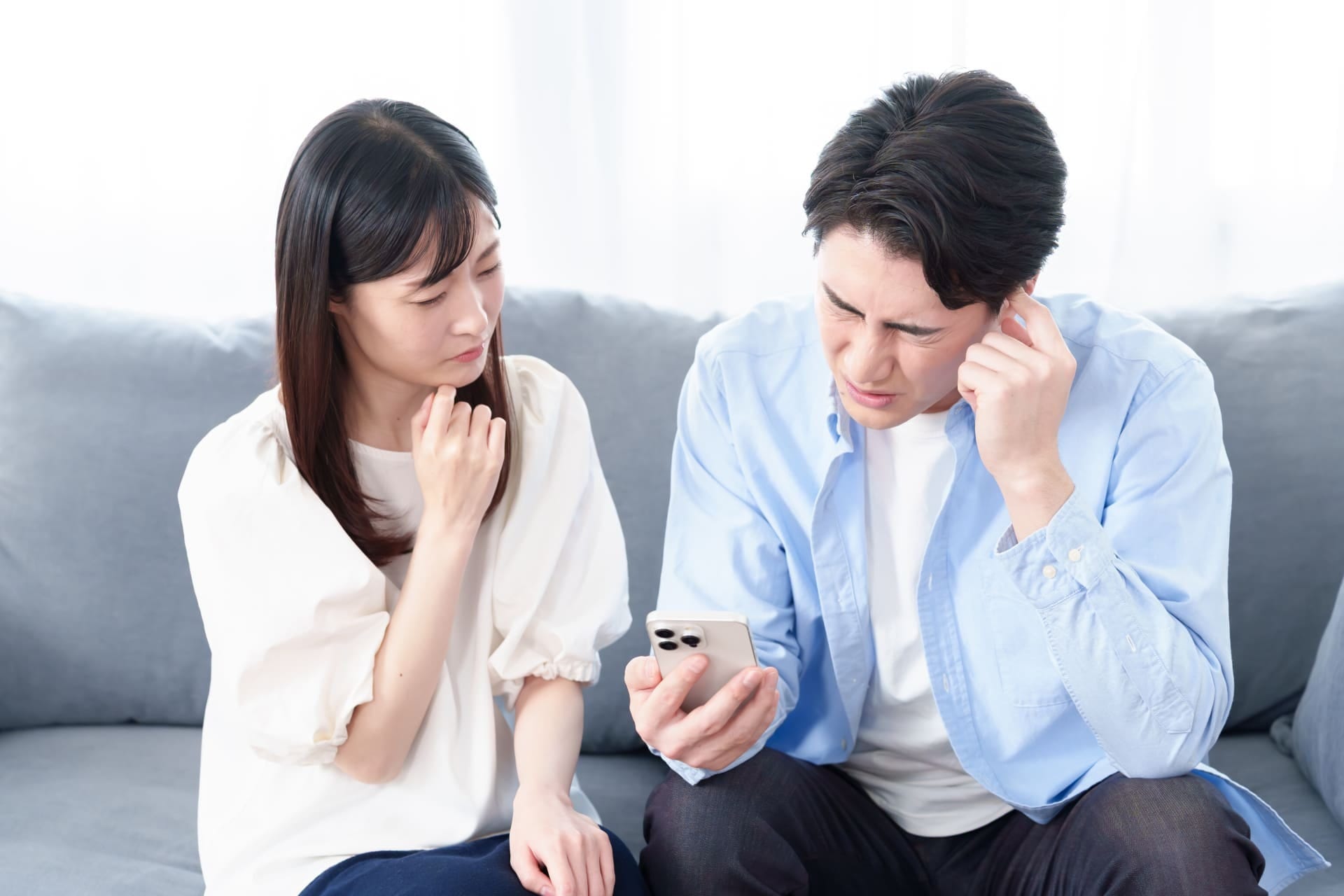 スマートフォンを見ながら悩む夫婦
