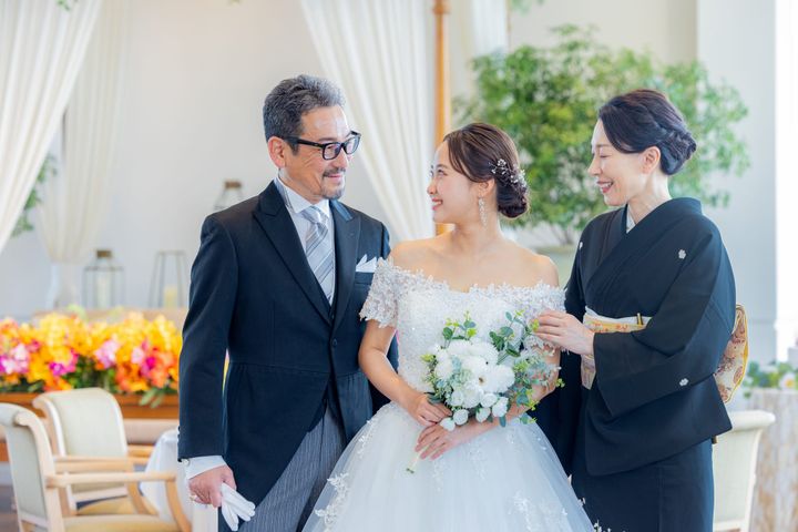 結婚式で白いウエディングドレスの新婦と並んで立つ両親
