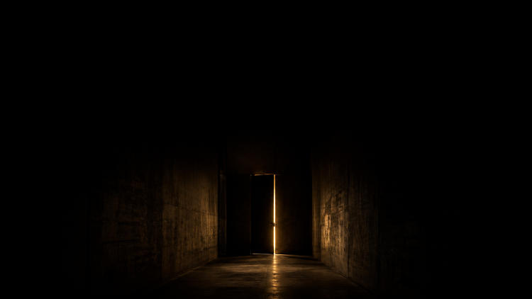 A dark corridor with a sliver of warm gold light from a door ajar — Before You Say No to Rural, a Golden Scalpel Resident Corner guide.