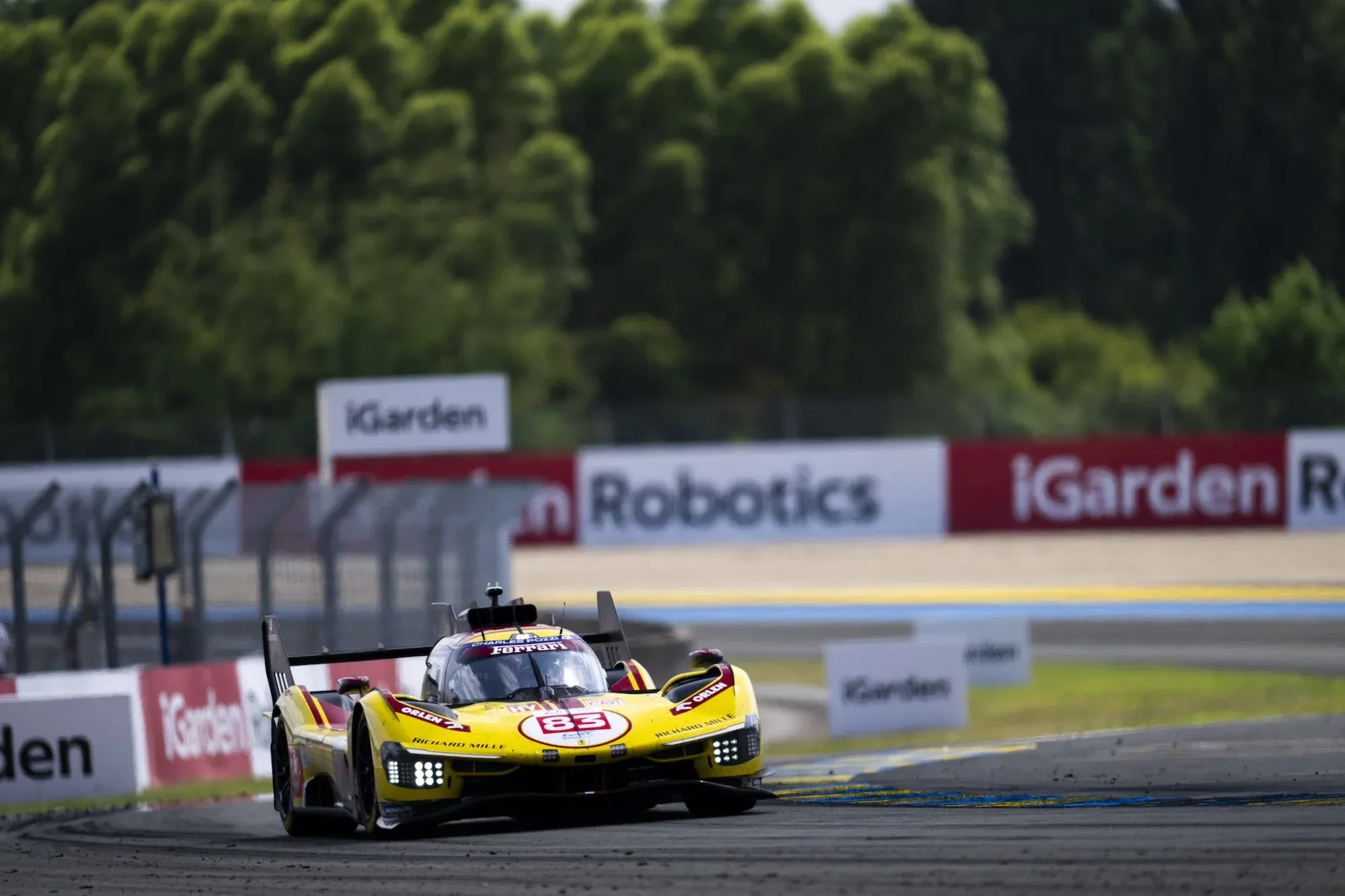 The yellow #83 AF Corse Ferrari 499P at Le Mans, in the day time, turning into a left hand corner