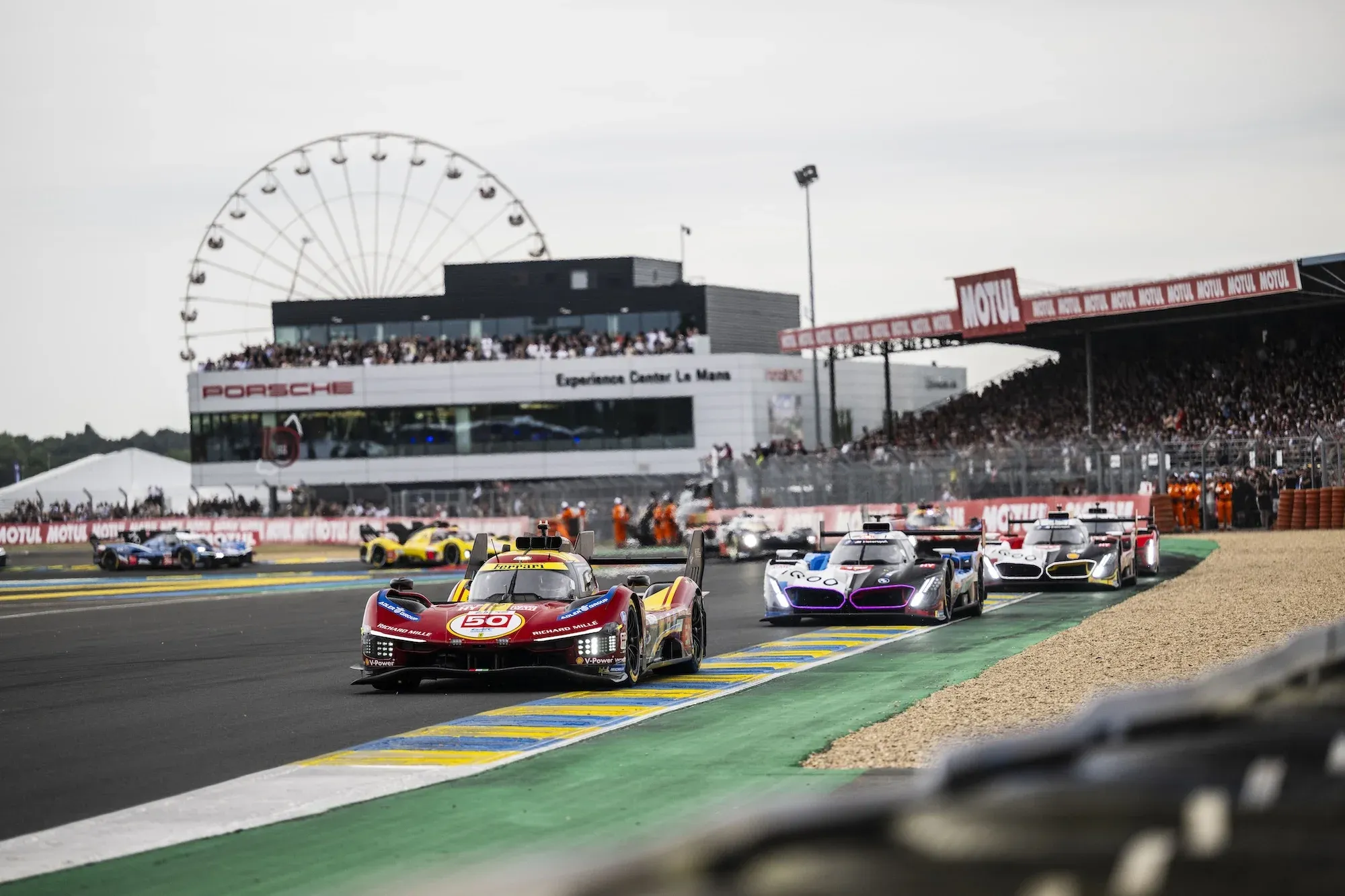 #50 Ferrari 499P leading other Hypercars coming out of the Ford Chicane at Le Mans, in the daylight