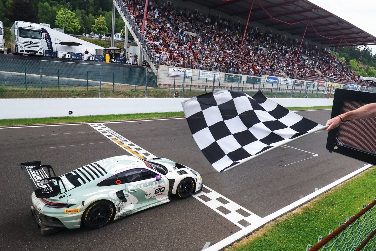 A very light green and white Porsche 911 GT3 R Evo crossing the finishing line at Spa-Francorchamps to win the Spa 24 Hours, with a chequered flag being waved and full grandstands