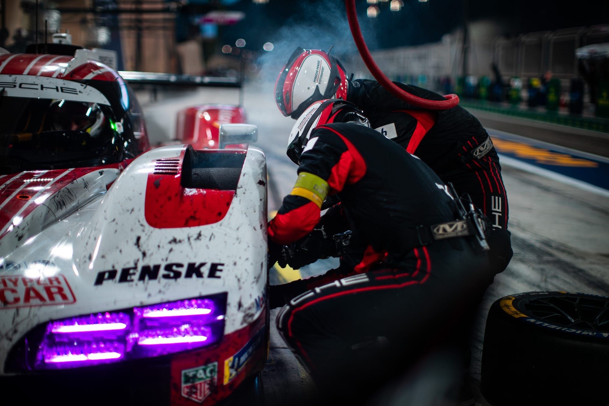 A Porsche 963 has its left front wheel and tyre changed at a pitstop at the 2026 8 Hours of Bahrain. The Penske logo is visible on the car's front bodywork. Bahrain