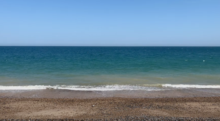 picture of shingle beach, small wave hitting the beach with sea and sky in the distance