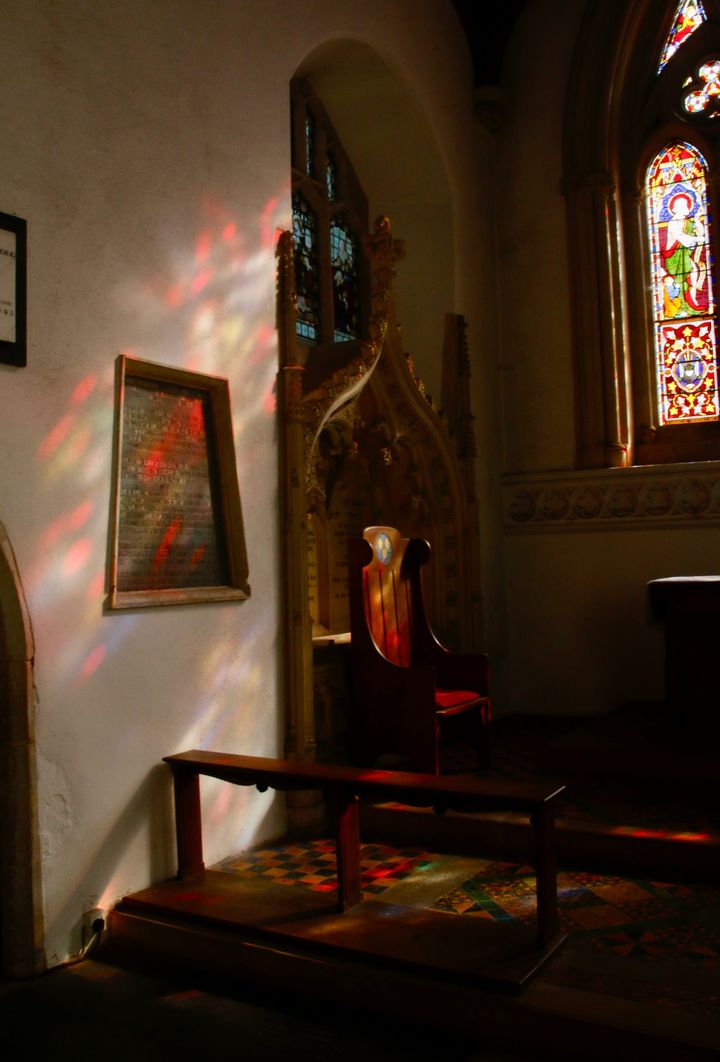 interior of a church, sun shining through a stained glass window casts colour light on to a wall and chair