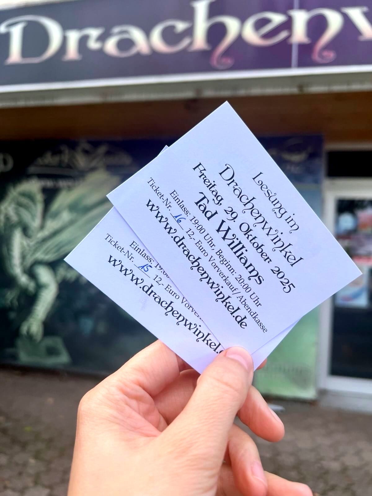 Hand, die Tickets für eine Lesung von Tad Williams am 29. Oktober 2025 hochhält vor dem Drachenwinkel in Dieflen