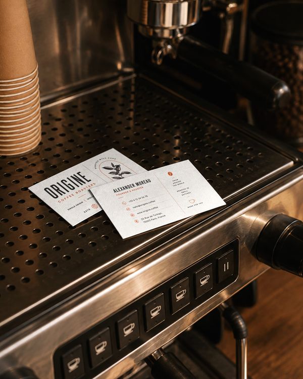 Business card mockup featuring elegant coffee roaster branding displayed on a stainless steel espresso machine, perfect for showcasing business cards, café identity, and specialty coffee bran