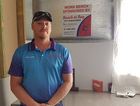 Ben Andrews of Beach to Bay Pest Management proudly standing in front of the workbench his company sponsored