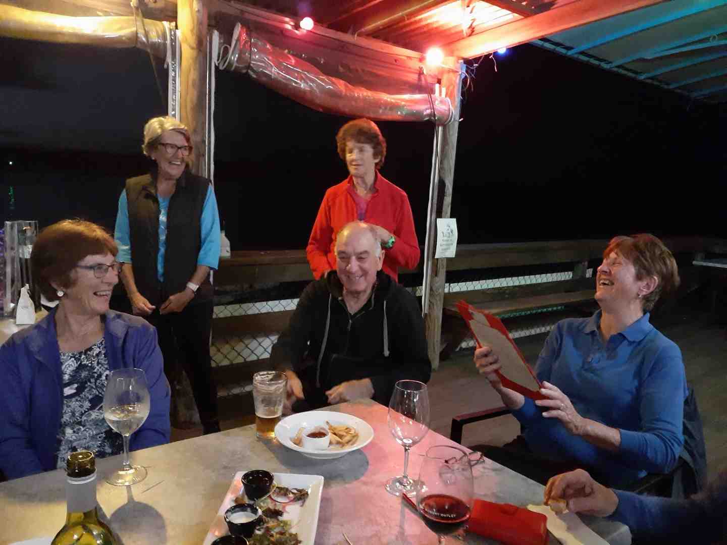 Octogenarian Norma Sanderson celebrating with fellow Dragons and friends at TCB Yacht Club: Andra Casey, Pam Corey, Vic Vella, Elaine Dimmock, and Norma, reading her handmade birthday card