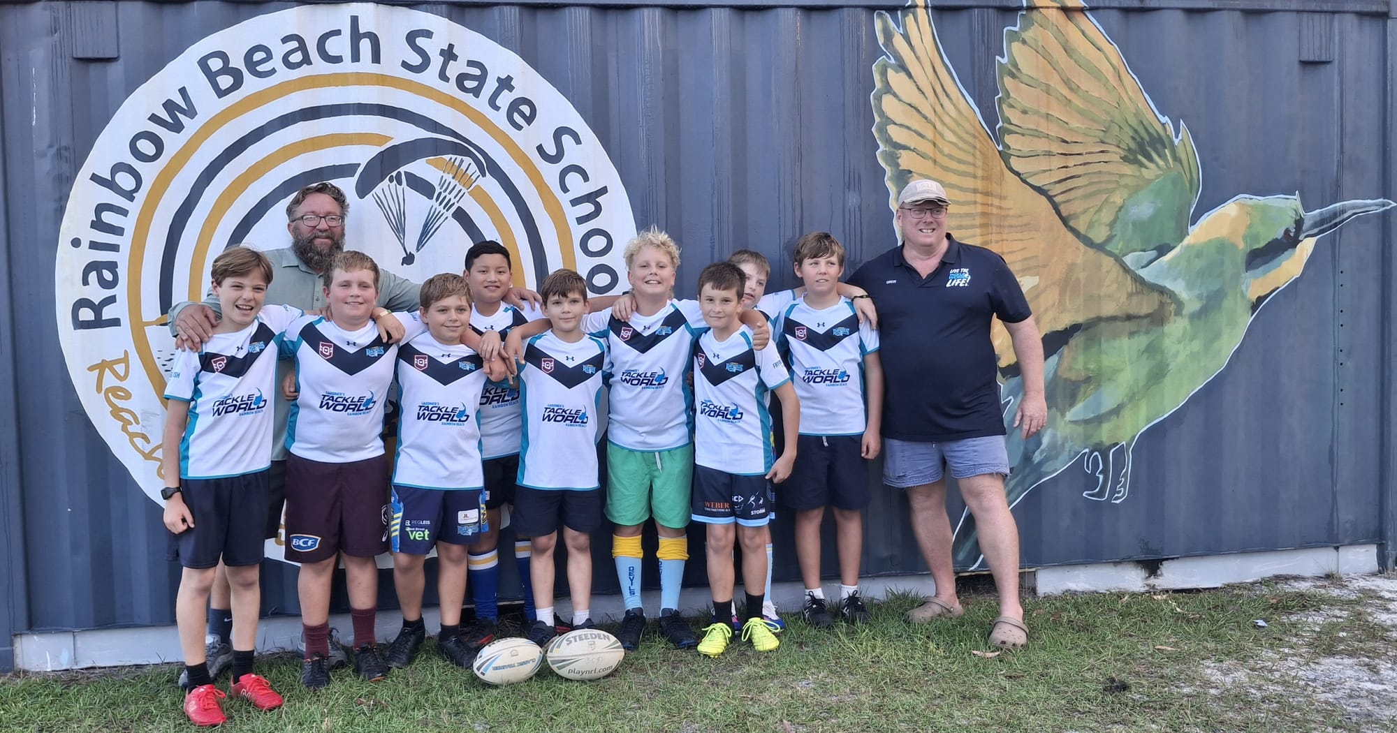 Rainbow Beach Junior Rugby League players proudly display their brand new jerseys. Pictured with Coach Steve Bennett and major sponsor Drew Gardiner from Rainbow Beach Tackle World.