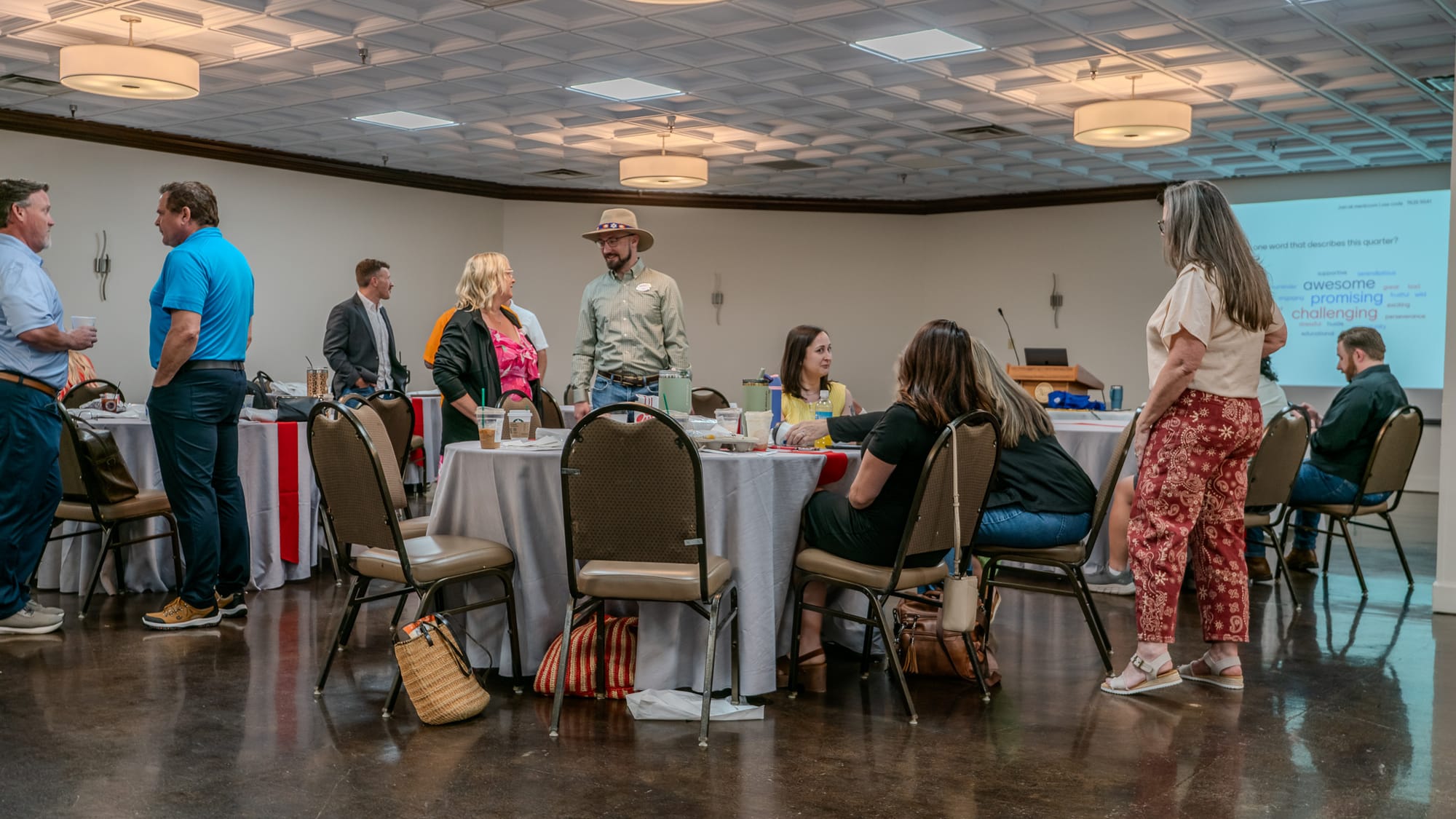 Team members networking before the Town Hall with a word cloud on the projector screen