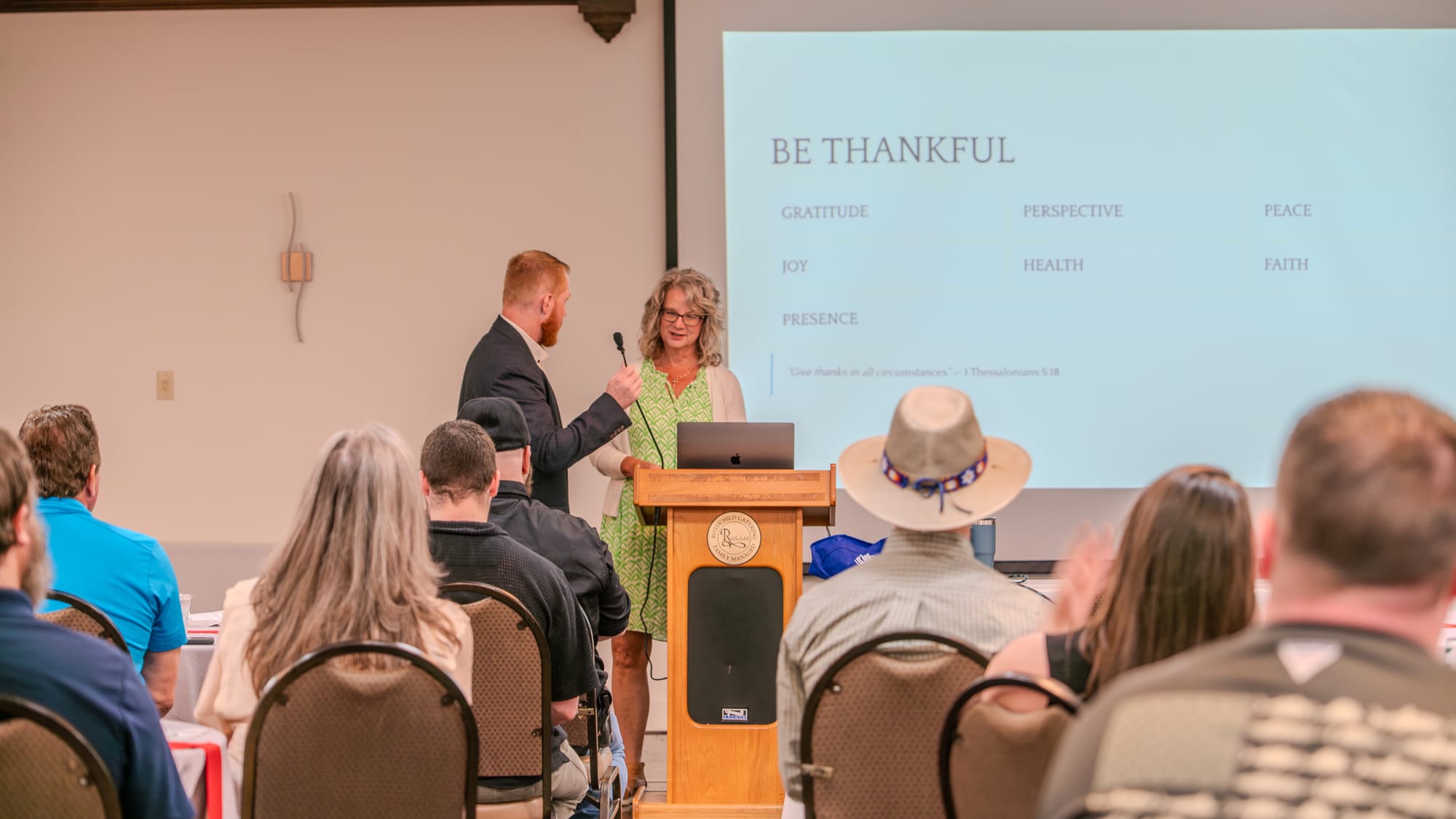 Presenter at the podium with Be Thankful slide displayed
