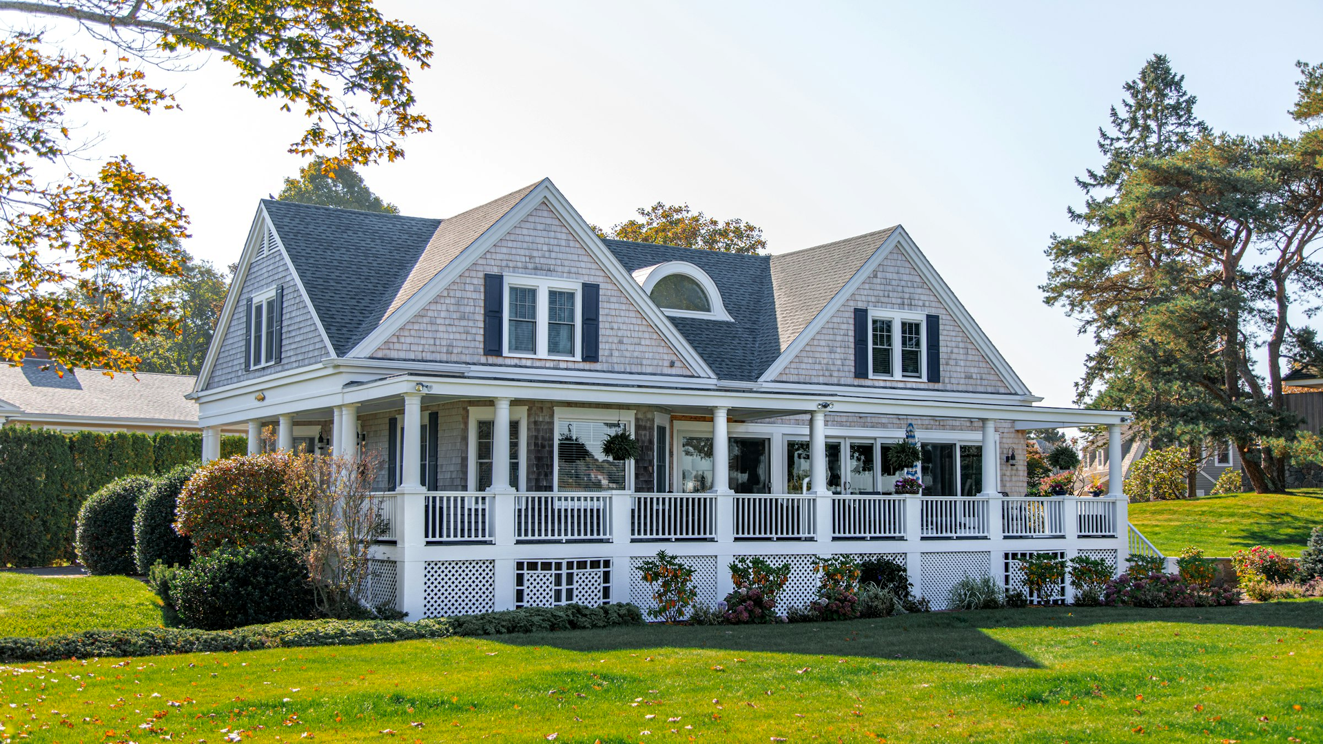 Empty shingled house with a wraparound porch and lawn under a clear sky, with no people, logos, or overlay text