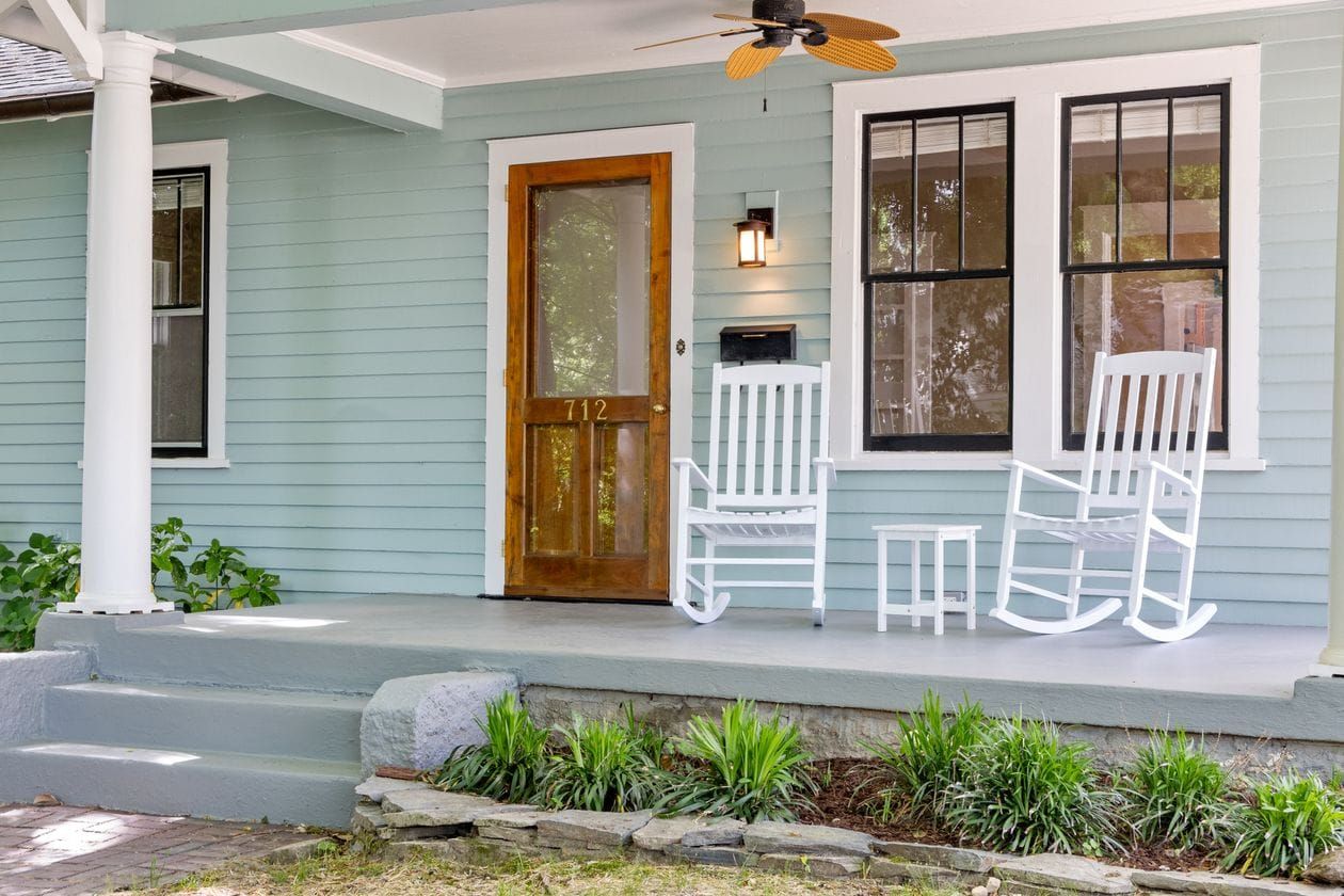 Inviting front porch featuring white rocking chairs and a wooden door, perfect for relaxation.