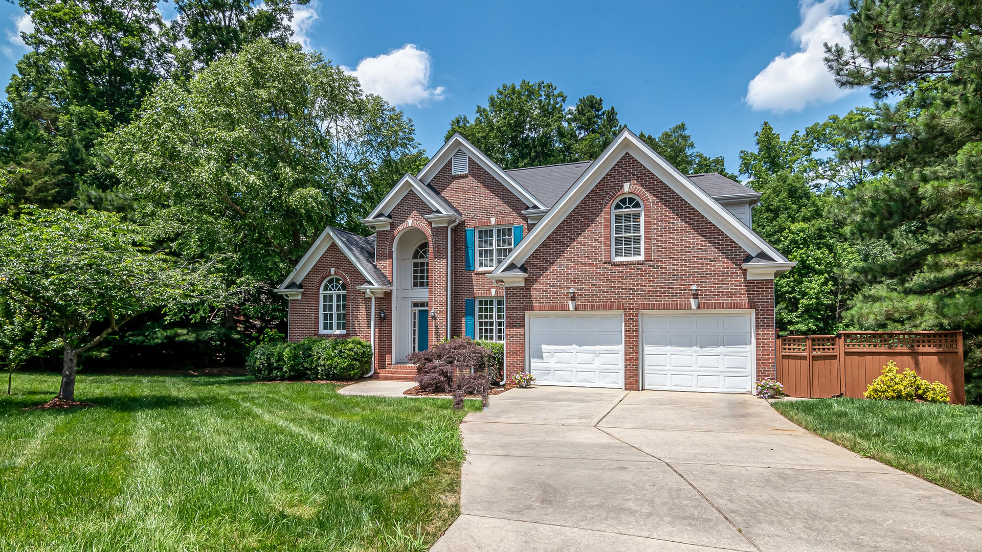 A two-story red brick house with a double garage, long driveway, and green lawn