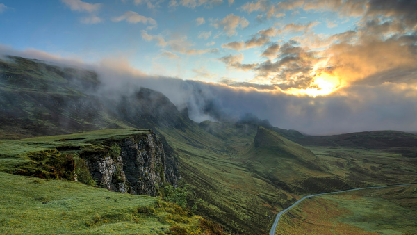 Mist-covered mountain valley at sunrise with a winding road and no people, logos, or readable signs