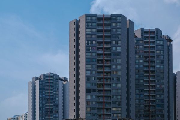 Photoreal low-angle view of a modern mid-rise apartment building with dark cladding and balconies against a blue sky, no people, logos, or text