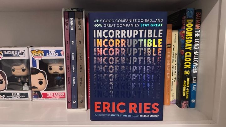 Incorruptible on a bookshelf surrounded by Funko Pops, graphics novels and other books
